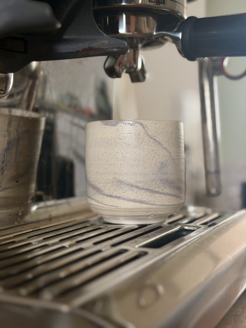 Marmorierter heller Becher unter einer Espressomaschine