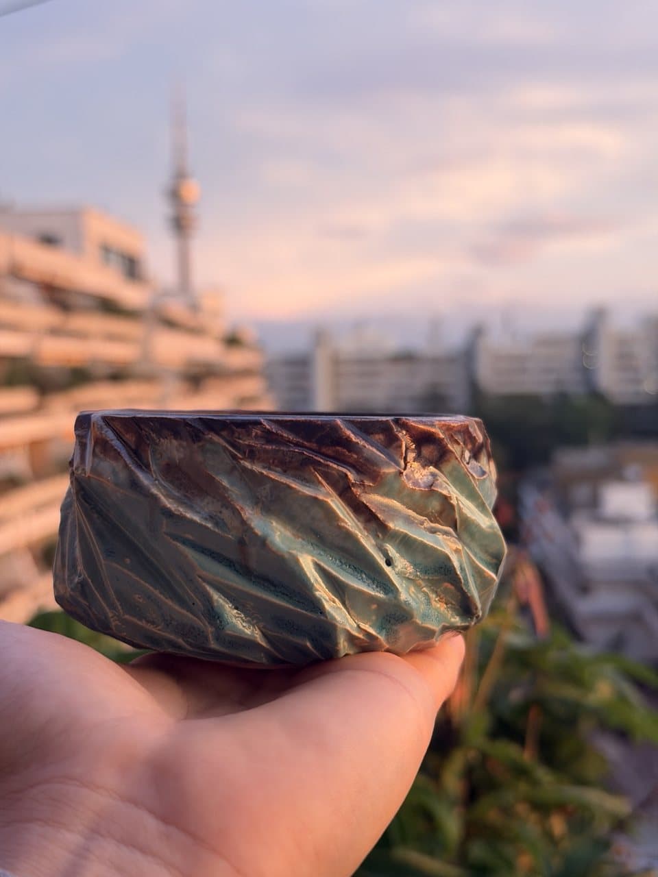 Facettierte grün glasierte Schale, dahinter der Münchner Olympiaturm